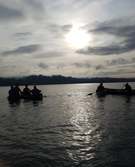 Silhouettes of canoeing students paddling across a calm loch at dusk under a cloudy sky. Silhouettes of canoeing students paddling across a calm loch at dusk under a cloudy sky.